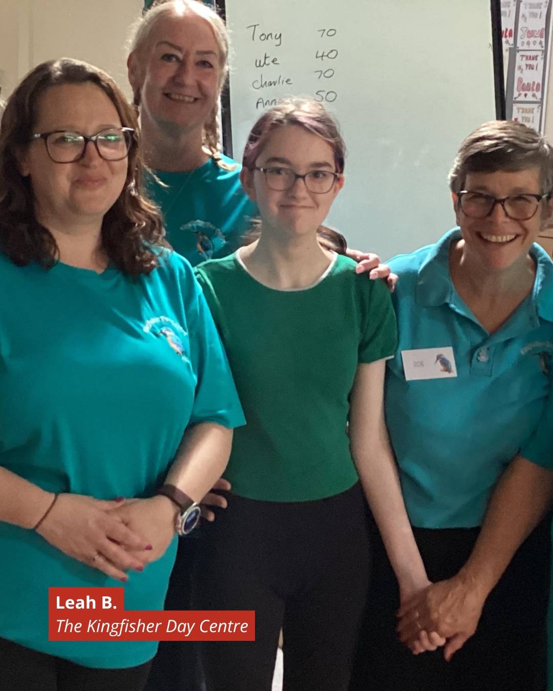 Group of four smiling women wearing teal tops, posing indoors at The Kingfisher Day Centre, Leah B. visible on a red label in the corner.