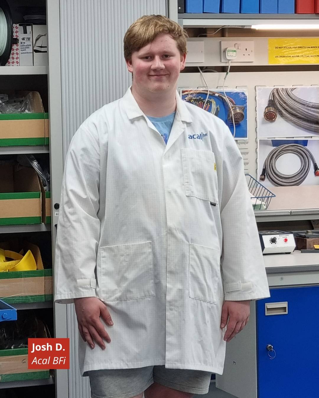 Young man with short blond hair in a white lab coat standing in a workshop with cables and tools visible; badge reads Josh D., Acal BFi.