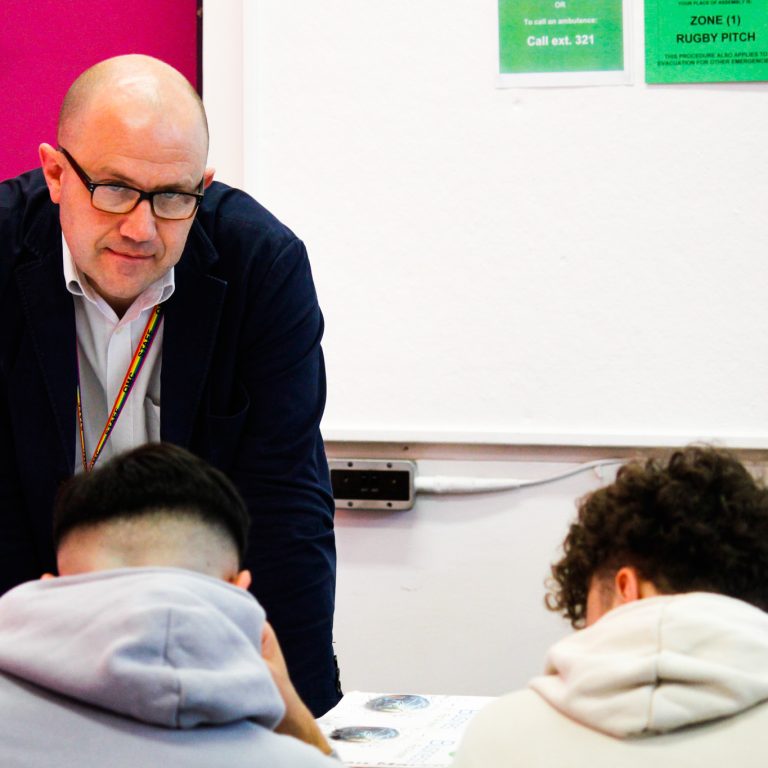 A teacher helping two students in a Business Class at Queen Mary's College.