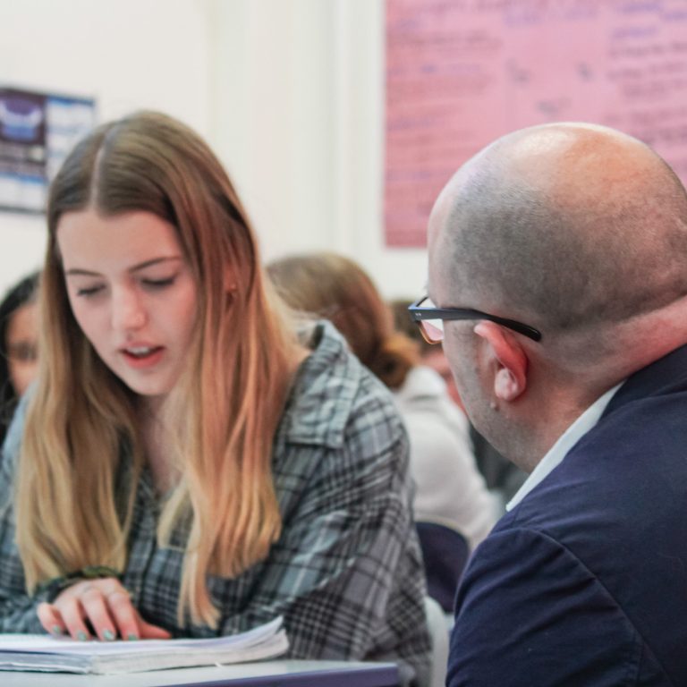 A Business teacher discussing a task with a student in a classroom at Queen Mary's College.