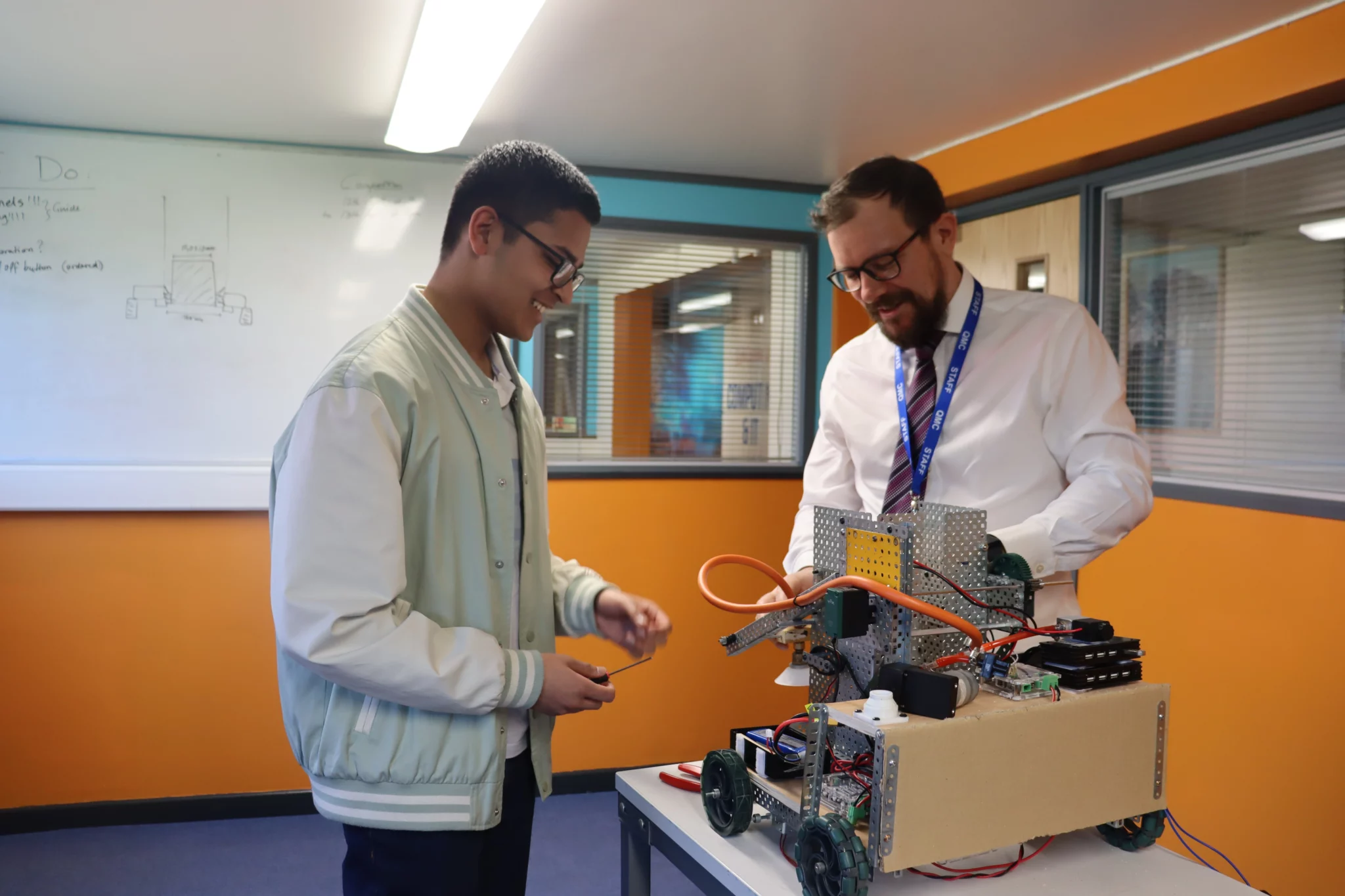 A student working on building a robot with a teacher.