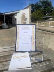 A glass award, a certificate in a frame and a leaflet on a wooden bench outside
