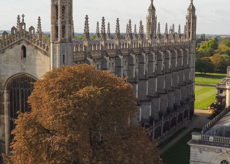 A wide aerial view of King's College Chapel and Cambridge University buildings under a bright sky.