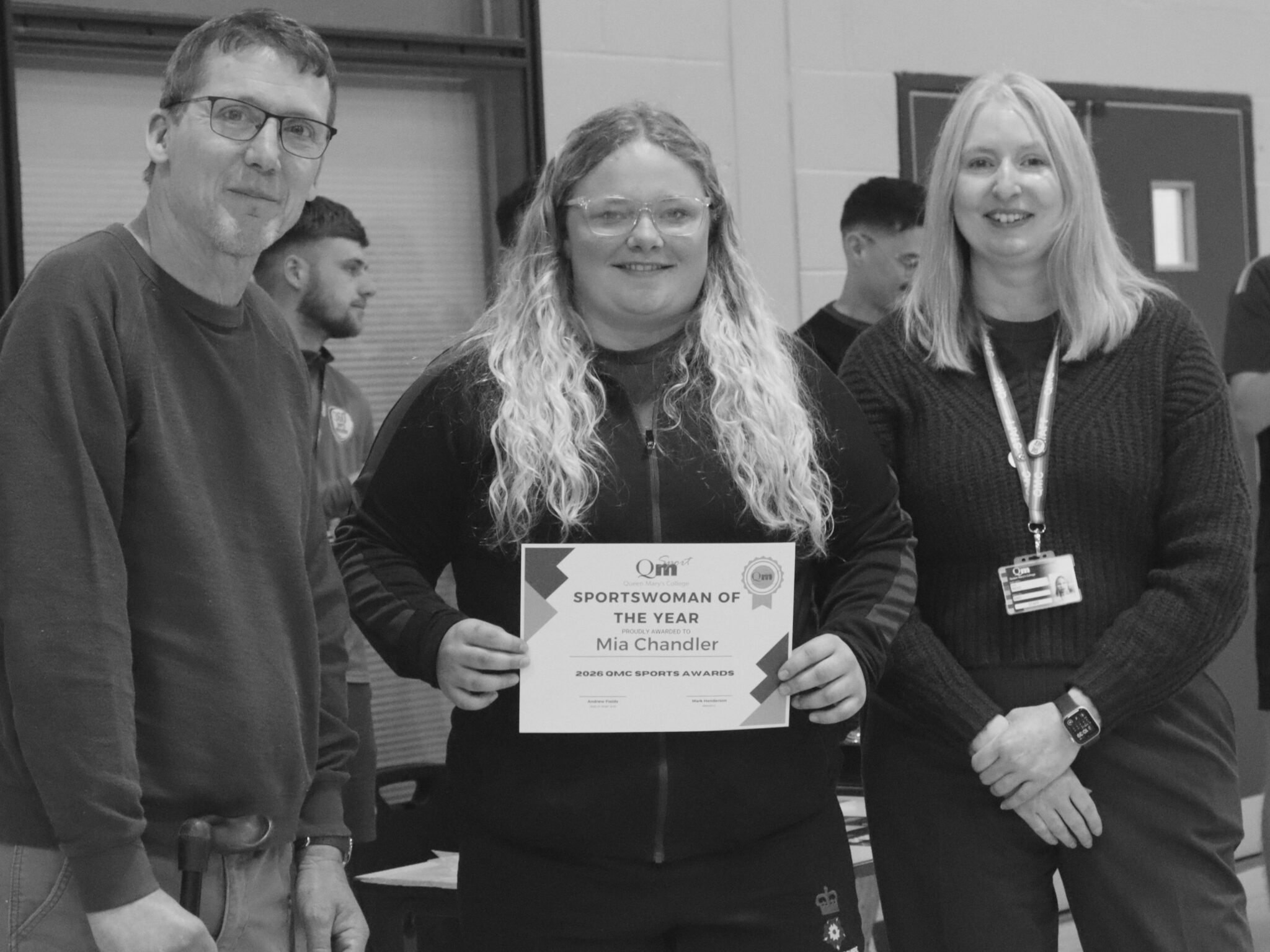 Three adults pose indoors; center woman holds a 'Sportswoman of the Year' certificate, Mia Chandler, flanked by a man on her left and a woman on her right.
