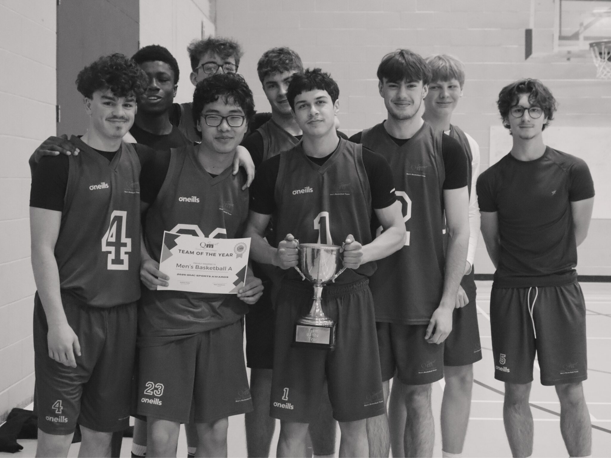 Basketball teammates pose together in a gym, holding a certificate and a trophy after an award.