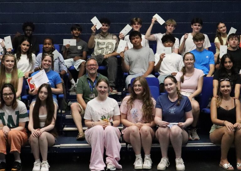 Large group of students on blue bleachers holding certificates, posing for a class photo after an event.