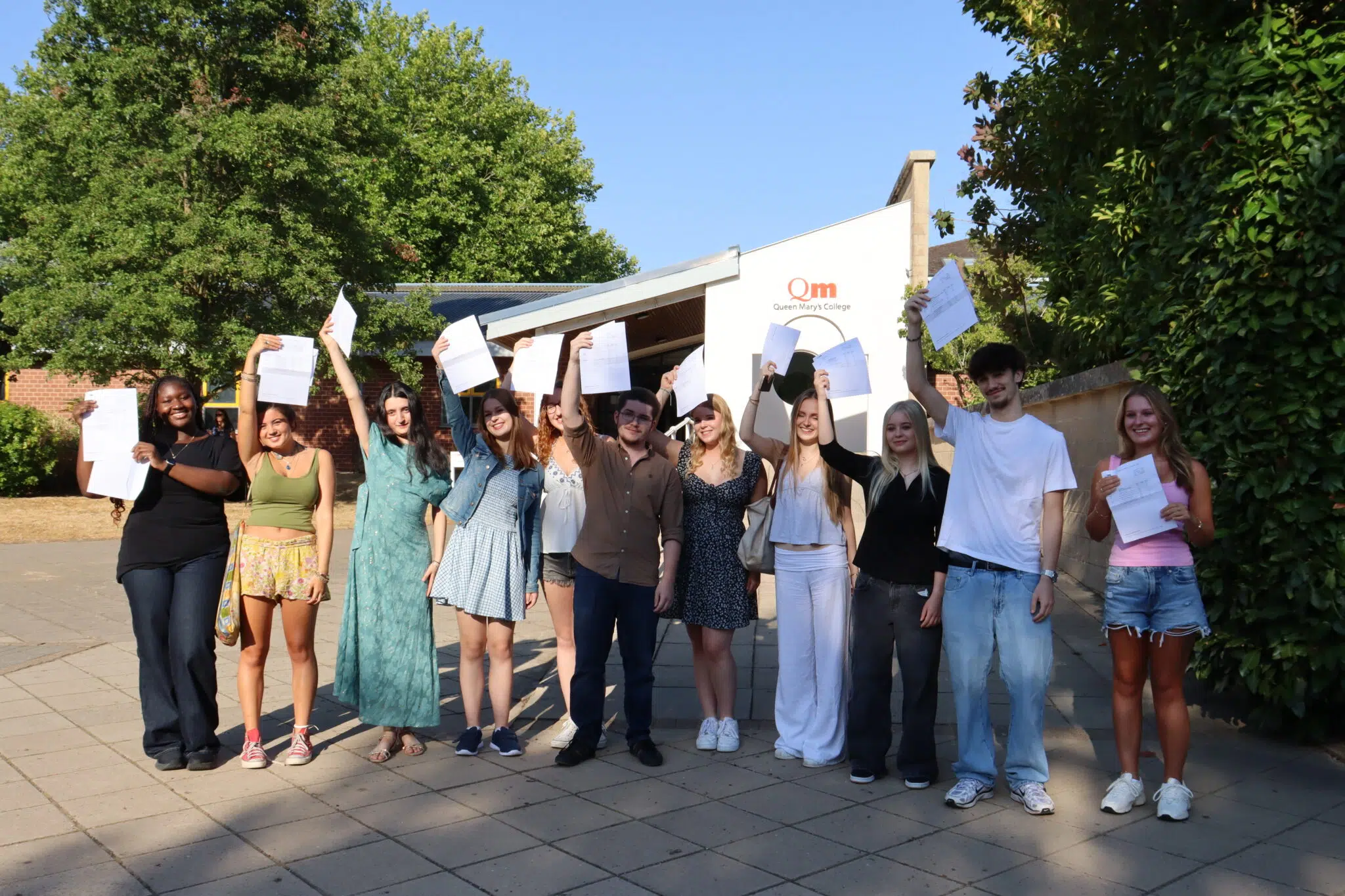 Group of diverse students celebrating A Level Results Day, in front of Queen Mary's College