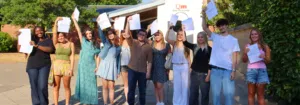 Group of diverse students outside Queen Mary’s College proudly holding up their papers in celebration of graduation/achievement day.