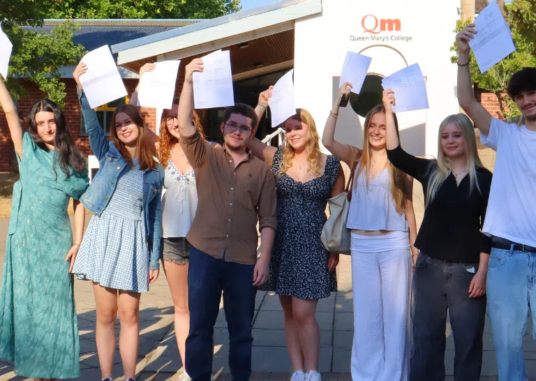 Group of diverse students outside Queen Mary’s College proudly holding up their papers in celebration of graduation/achievement day.