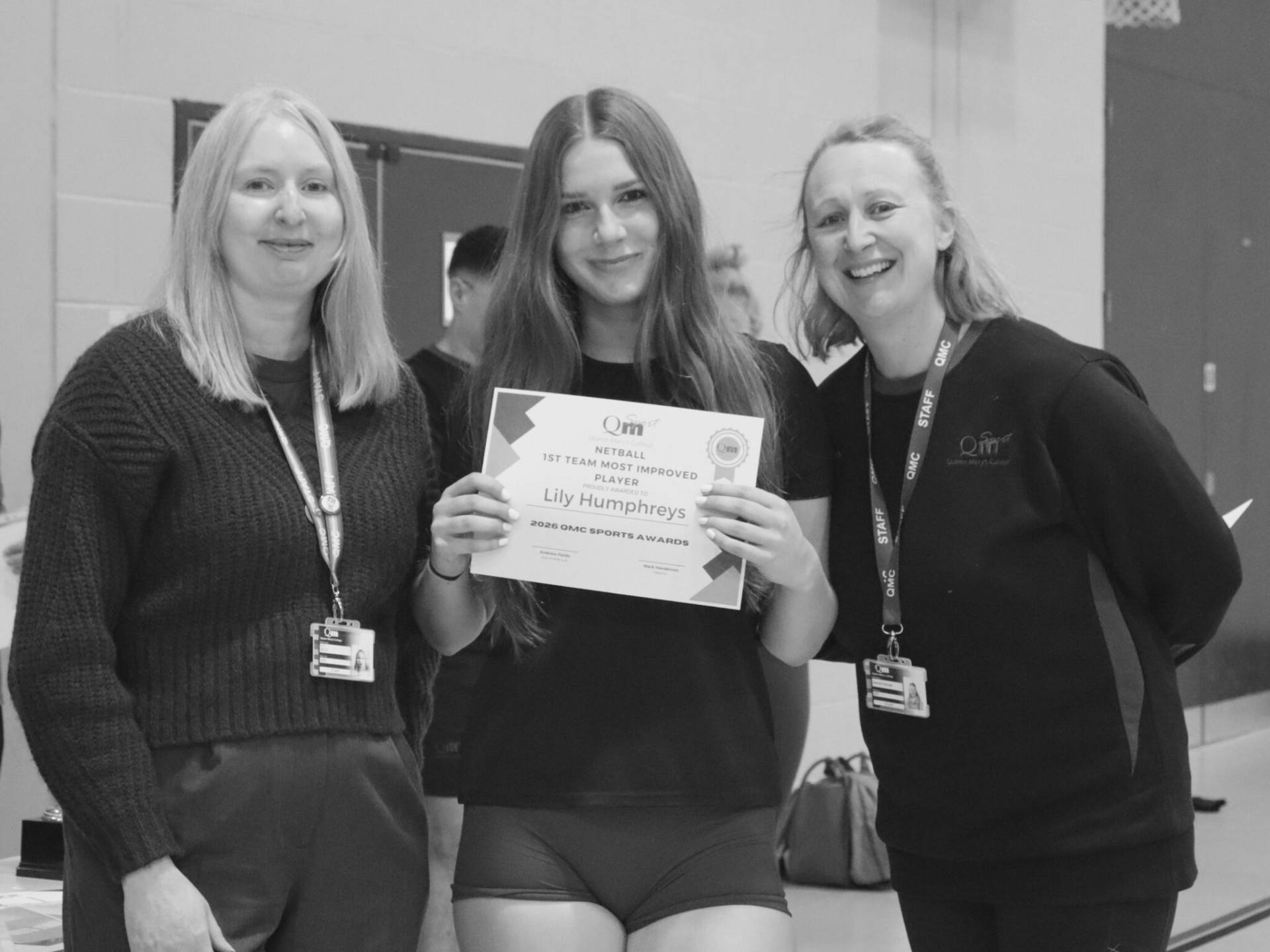 Three smiling women pose indoors; the center woman holds an award certificate.
