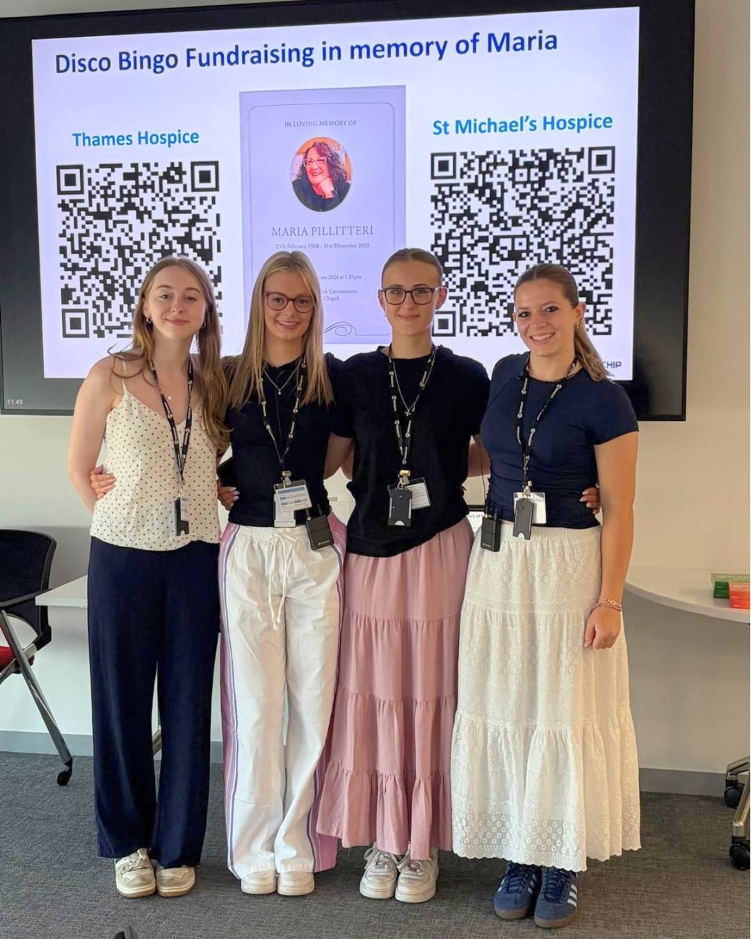 Four women pose at a disco bingo fundraiser in memory of Maria, standing in front of a memorial poster and two QR codes for Thames Hospice and St Michael's Hospice.
