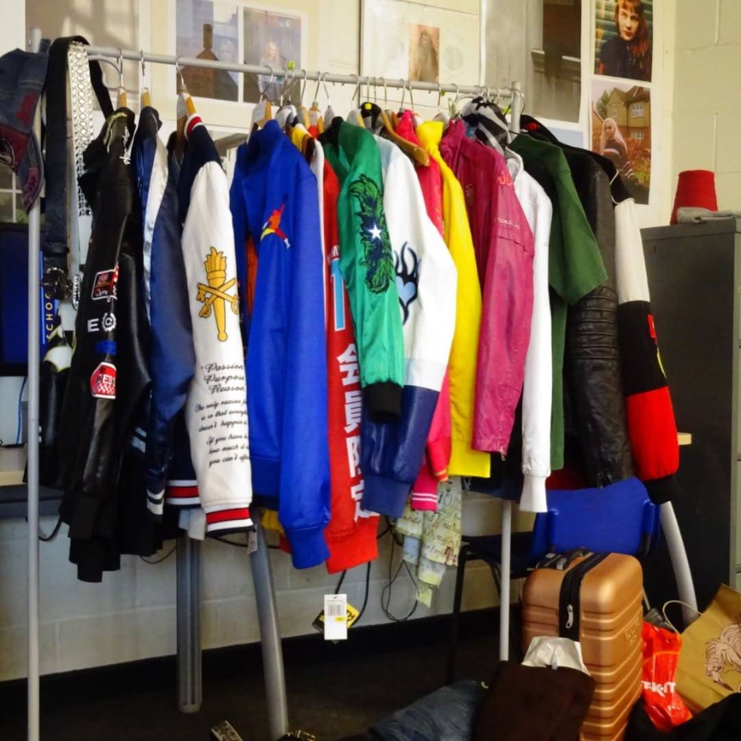 Colorful jackets and coats hang on a metal rack in a room, with suitcases and bags on the floor nearby.